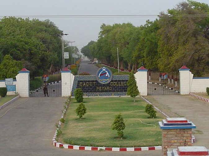 The main gate of Cadet College Petaro seen from the approach road, with the college crest on the gate wall.